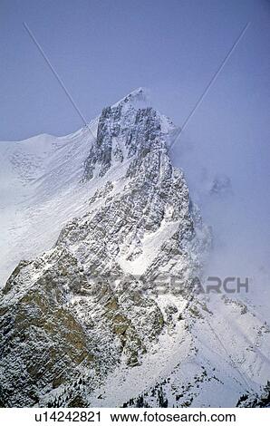 Stock Image -  close up snow capped rocky mountain shrouded in mist. Fotosearch