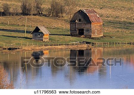Stock Image - horozontal image old barn lake shore bathed in warming glow. Fotosearch