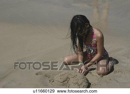 Stock Photo -  beach girl sun little focused digging in sand. Fotosearch