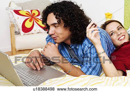 Stock Photo -  woman computer man laptop young leaning back bed. Fotosearch