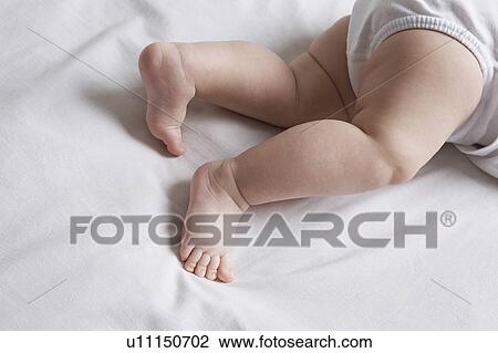 Stock Image - Baby (1-6 months) lying on bed, low section. Fotosearch