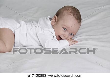 Stock Image - Baby (1-6 months) lying on front on bed, portrait. Fotosearch