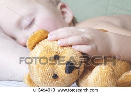 Stock Image - Baby boy lies with teddy bear sleeping. Fotosearch