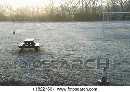 Stock Photo - Bench and bollards on empty soccer field at sunset. Fotosearch