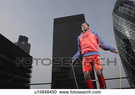 Stock Image - Boxer skipping on skipping rope, amongst buildings, low angle view, London, England. Fotosearch