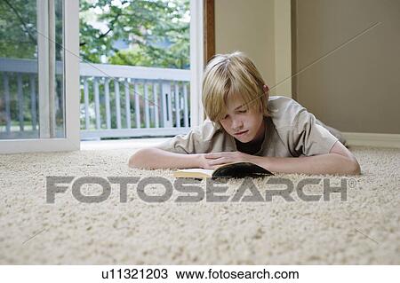 Stock Image - Boy (10-12) lying on carpet reading book. Fotosearch