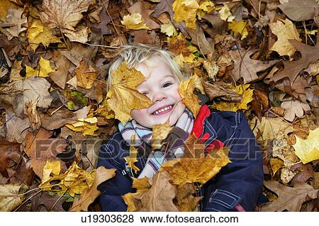 Stock Photo - Boy (3-4) Lying on ground covered in autumn leaves. Fotosearch