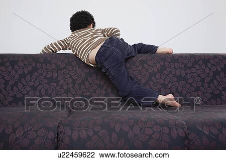 Stock Image - Boy (5-6) climbing over sofa. Fotosearch