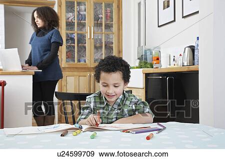 Boy (5-6) colouring in colouring book, mother using laptop in background View Large Photo Image Stock Photo - Boy (5-6) colouring in colouring book, mother using laptop in background. Fotosearch