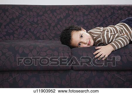 Stock Image - Boy (5-6) lying on sofa, portrait. Fotosearch