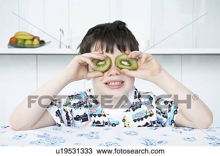 Stock Image - Boy (5-6) putting kiwi slices to eyes. Fotosearch