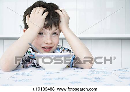 Boy (5-6) sitting at table with bowl in front of face View Large Photo Image Stock Photo - Boy (5-6) sitting at table with bowl in front of face. Fotosearch