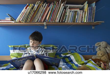 Boy (5-6) sitting on bed, reading book View Large Photo Image Stock Photo - Boy (5-6) sitting on bed, reading book. Fotosearch