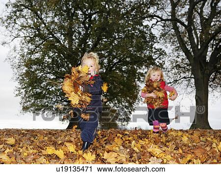 Stock Image - Boy and girl (3-4) playing in autumn leaves. Fotosearch