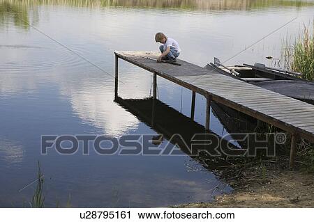Stock Image - Boy sitting at end of jetty by lake. Fotosearch