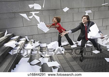 Stock Image - Busines man and woman catching falling paperwork on steps. Fotosearch
