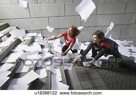 Stock Image - Busines man and woman catching falling paperwork on steps. Fotosearch
