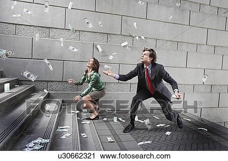 Stock Image - Busines man and woman catching falling money on steps. Fotosearch
