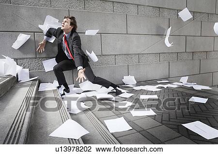 Stock Image - Busines man catching falling paperwork on steps. Fotosearch