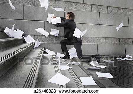 Stock Image - Busines man catching falling paperwork on steps. Fotosearch
