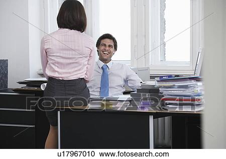 Stock Image - Business man and woman talking in office, smiling. Fotosearch