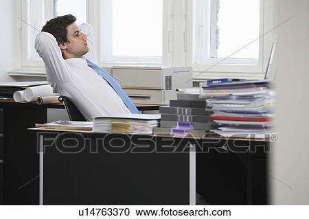 Stock Image - Business man relaxing at desk in office. Fotosearch