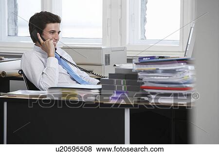 Stock Photo - Business man using telephone at desk in office, smiling. Fotosearch