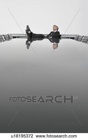 Stock Image - Business man with feet up on table in conference room. Fotosearch