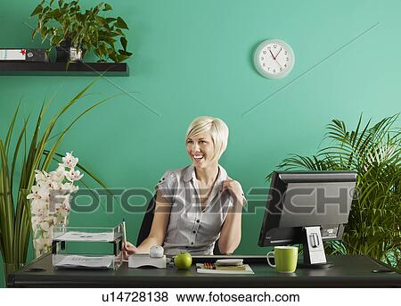 Stock Photo - Business woman behind desk in office full of potted plants. Fotosearch