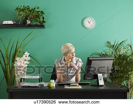 Stock Photograph - Business woman behind desk in office full of potted plants. Fotosearch