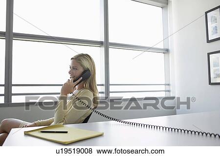 Business woman using phone sitting at office desk, side view View Large Photo Image Stock Photo - Business woman using phone sitting at office desk, side view. Fotosearch