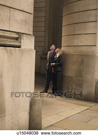 Stock Photo - Businessman and businesswoman standing at entrance to monumental building, looking up. Fotosearch