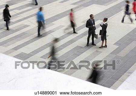 Stock Image - Businessman and businesswomen standing and talking in outdoor plaza, people passing, elevated view. Fotosearch