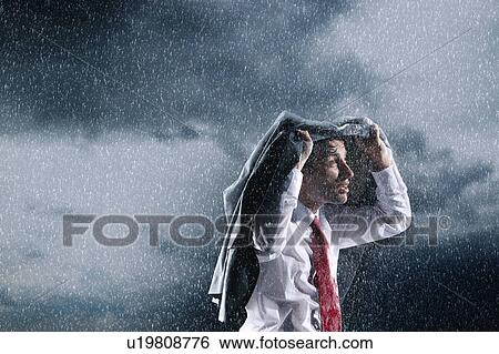 Stock Photograph - Businessman covering head with jacket during rainstorm. Fotosearch