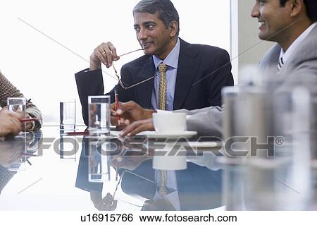 Stock Photograph - Businessman holding spectacles to mouth on business meeting, close-up. Fotosearch