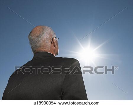 Picture - Businessman looking at sun, head and shoulders, back view. Fotosearch