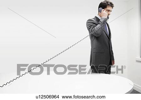 Businessman on Telephone by desk in office stretching receiver cord View Large Photo Image Picture - Businessman on Telephone by desk in office stretching receiver cord. Fotosearch