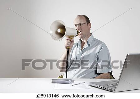 Stock Photograph - Businessman sitting at desk, speaking through megaphone. Fotosearch