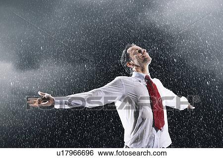 Stock Photograph - Businessman standing, arms spread facing incoming rain. Fotosearch