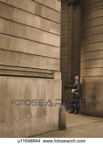 Picture - Businessman standing in entrance to monumental building, looking up. Fotosearch