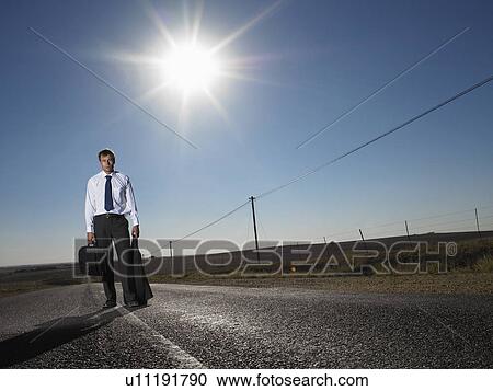 Stock Image - Businessman standing in middle of deserted road. Fotosearch