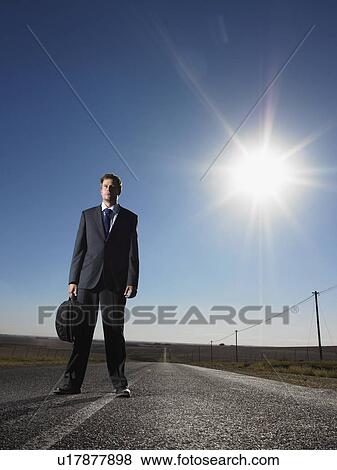 Stock Photo - Businessman standing in middle of deserted road. Fotosearch