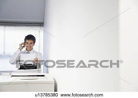 Stock Image - Businessman Talking on Cell Phone and receiving fax. Fotosearch