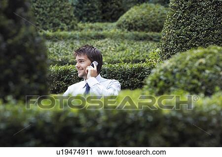 Businessman talking on cell phone in park garden, seem through hedges View Large Photo Image Stock Image - Businessman talking on cell phone in park garden, seem through hedges. Fotosearch
