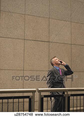 Stock Photo - Businessman talking on mobile phone, looking up. Fotosearch