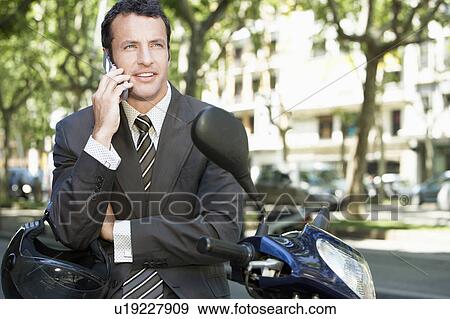 Stock Photo - Businessman using mobile phone by motorscooter on street. Fotosearch