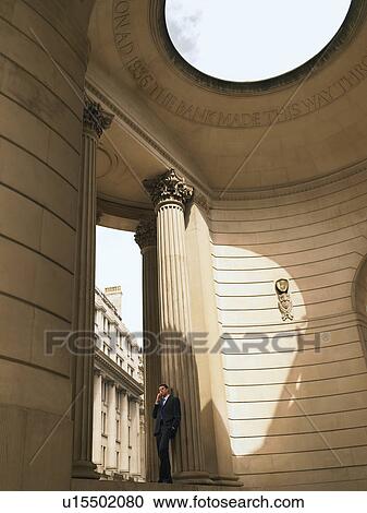 Stock Image - Businessman using mobile phone in neo-classical style building. Fotosearch
