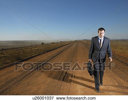 Stock Photo - Businessman walking down road in isolated landscape. Fotosearch