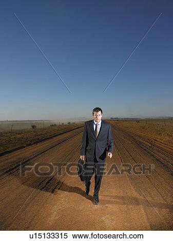 Stock Photography - Businessman walking down road in isolated landscape. Fotosearch
