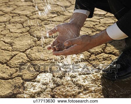 Stock Image - Businessman washing hands in desert, close-up of hands. Fotosearch